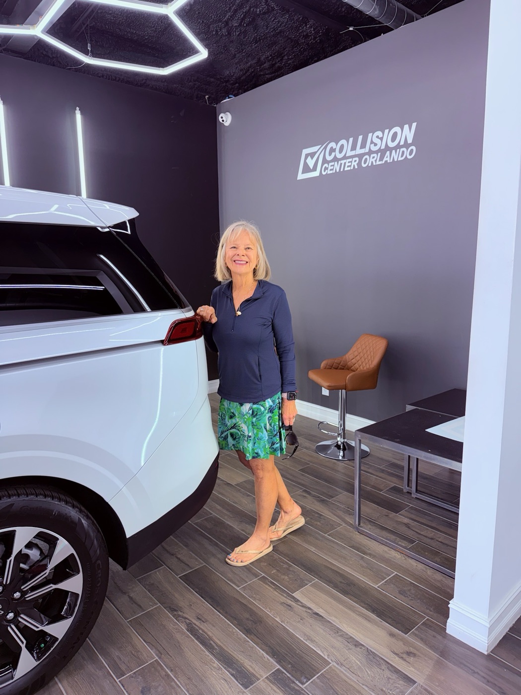 A happy Collision Center Orlando customer with her finished white SUV in the delivery showroom