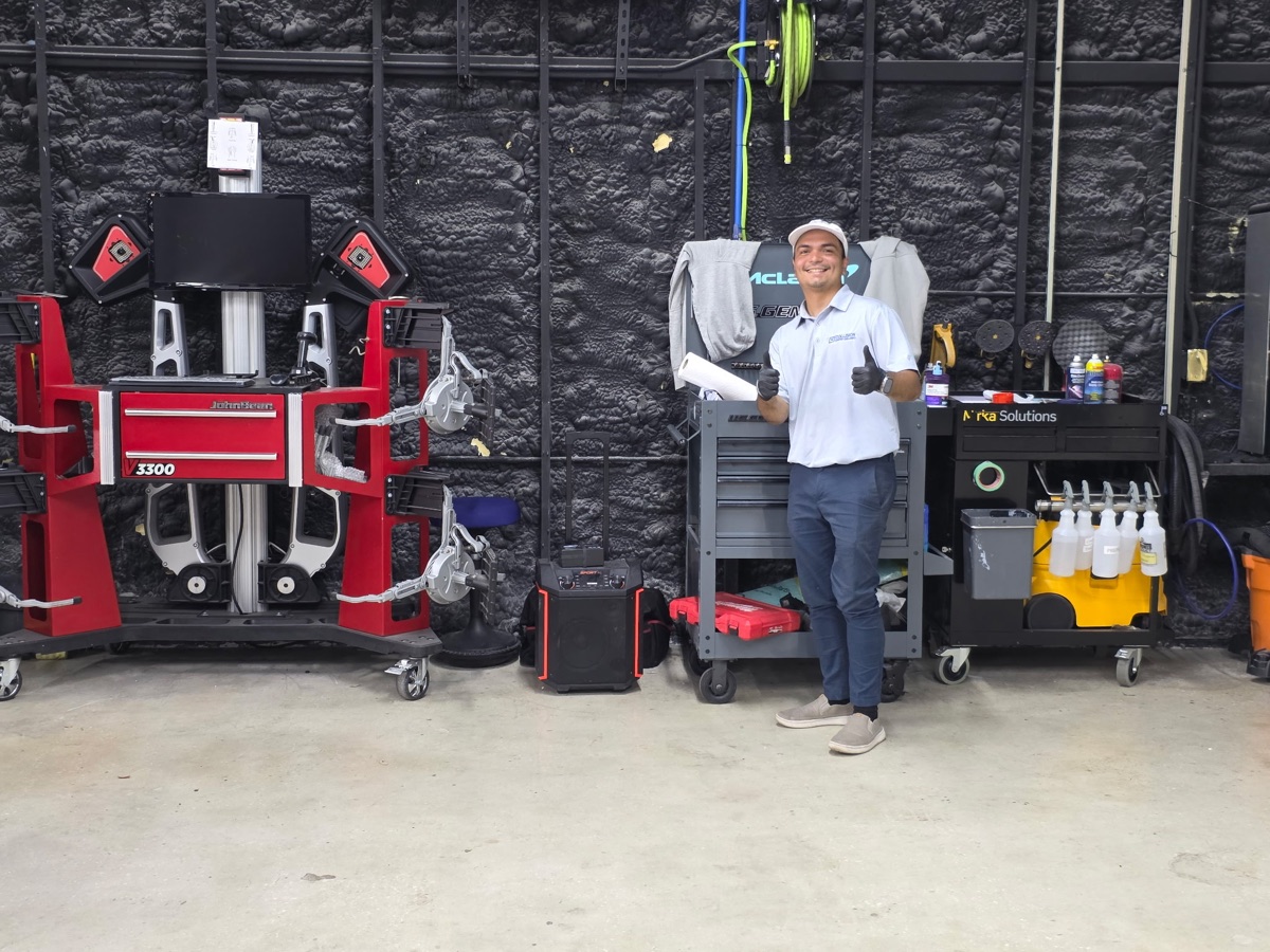 A uniformed Collision Center Orlando technician with wheel alignment and precision measuring equipment